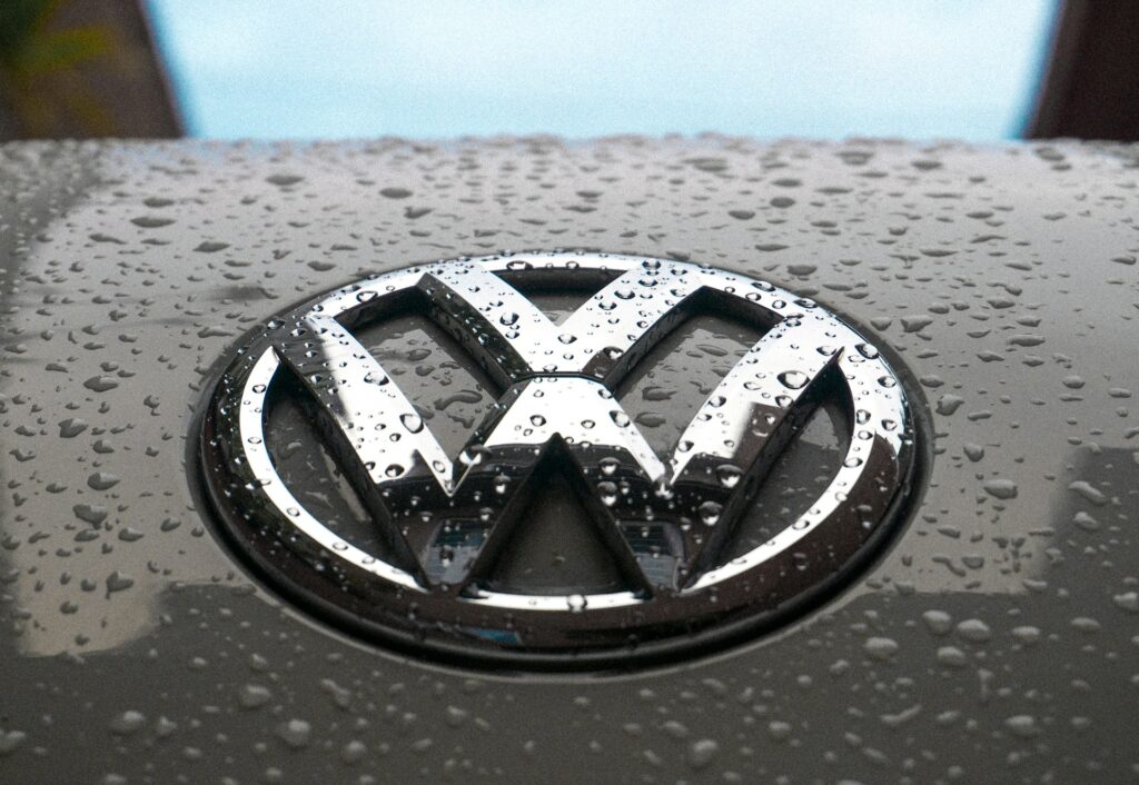 Close-up of a Volkswagen emblem with water droplets on a silver car surface. VW ID4 vs Tesla Model Y – comparing top electric SUVs in design and features.