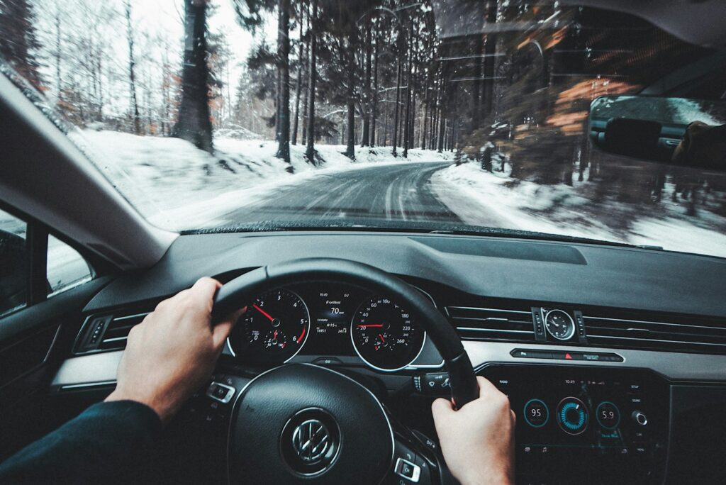 Driver steering a Volkswagen through a snowy forest road. VW ID4 vs Tesla Model Y – comparing driving experience, performance, and winter handling.
