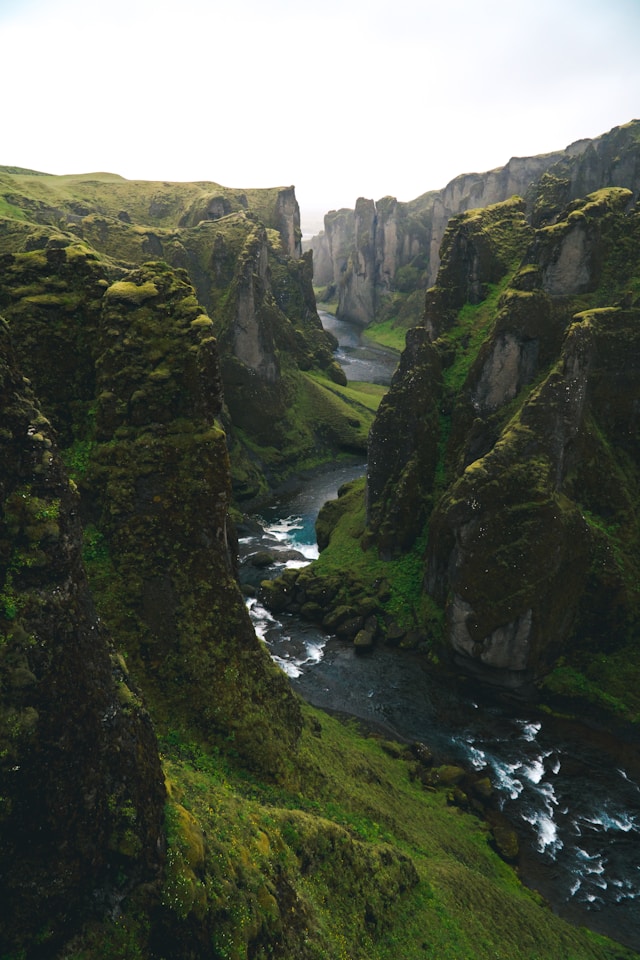 Aerial view of a winding river flowing through lush green cliffs in Iceland, showcasing the untouched natural beauty central to Iceland ecotourism.
