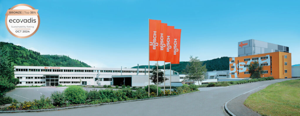 Busch Group headquarters with orange company flags, showcasing its EcoVadis bronze medal for sustainability, awarded in October 2024 for ranking in the top 35%.