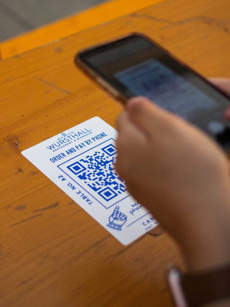 Person scanning a QR code on a table using a smartphone—demonstrating how digital features enhance business cards eco friendly with contactless interaction.