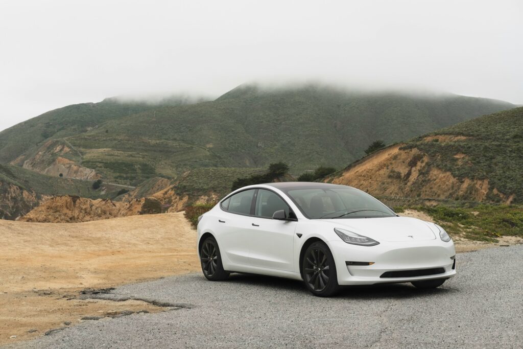 A white Tesla electric sedan parked against a misty mountain backdrop, illustrating the performance aspect in the kia niro ev vs tesla model y debate.







