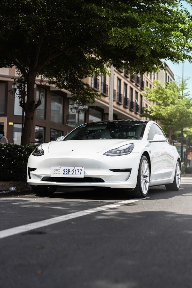 White Tesla Model 3 parked on a shaded city street, demonstrating real-world conditions related to how long can a Tesla sit without charging.
