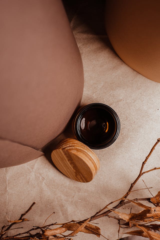 Top view of an amber glass container with a wooden bamboo lid on a neutral background with natural elements, demonstrating what to do with old candle wax by repurposing empty containers into stylish storage solutions for home decor.