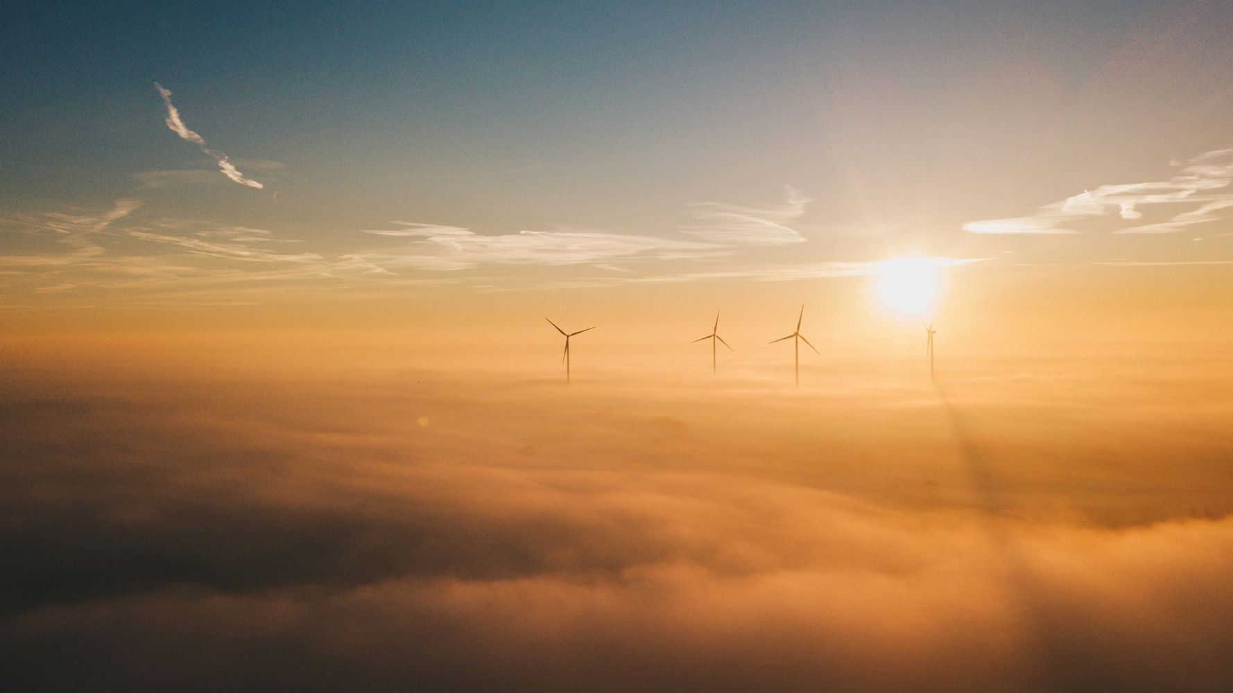 Wind turbines emerging through dense fog at sunrise, symbolizing the growing demand for renewable energy resources and sustainable power solutions.
