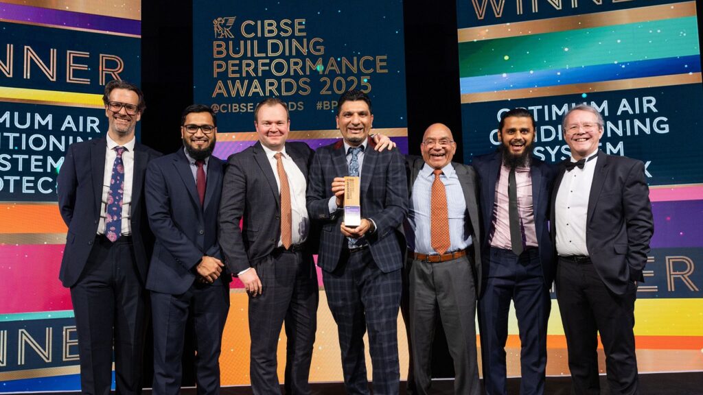 A team of researchers and industry professionals celebrate winning an award for energy efficiency solutions at the CIBSE Building Performance Awards 2025, holding a trophy in front of a colorful backdrop displaying "WINNER" and "Optimum Air Conditioning System.