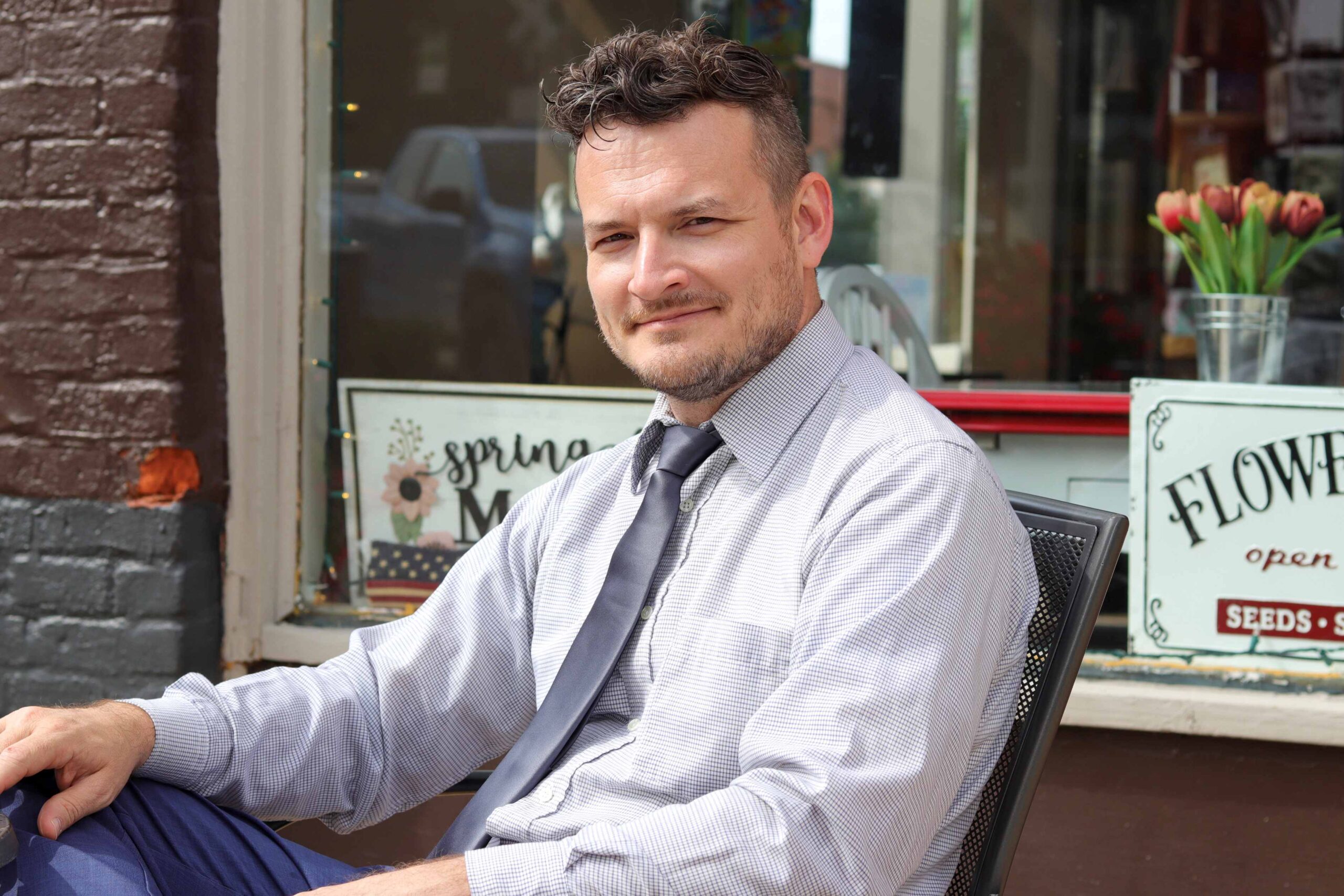 Philip Portman, CEO of Textdrip, sits outside a storefront with a confident expression, advocating how SMS reduces paper waste in business communication.