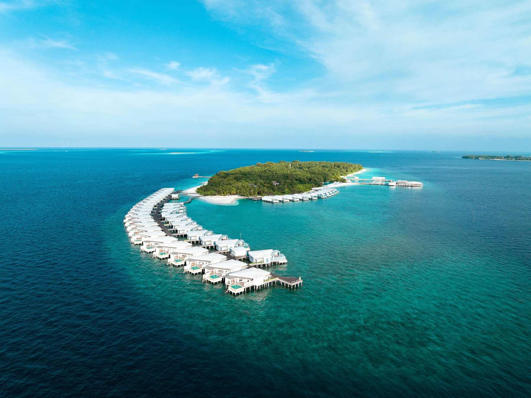 Aerial view of Amilla Maldives, a sustainable luxury resort Maldives, featuring overwater villas surrounded by turquoise ocean and lush island greenery.