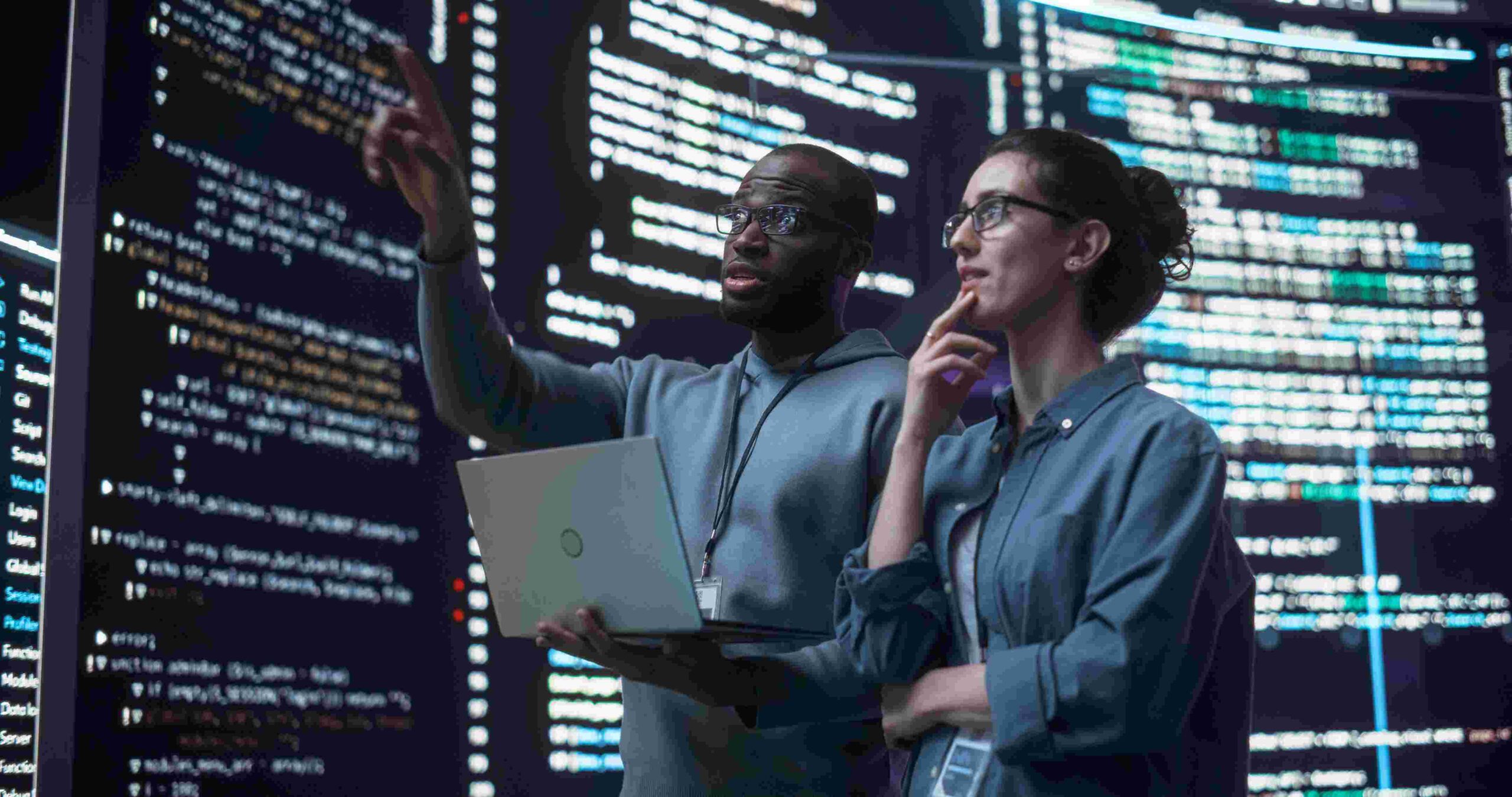 Two data analysts reviewing code on large screens, collaborating on digital solutions focused on maximising sustainable returns through technology.