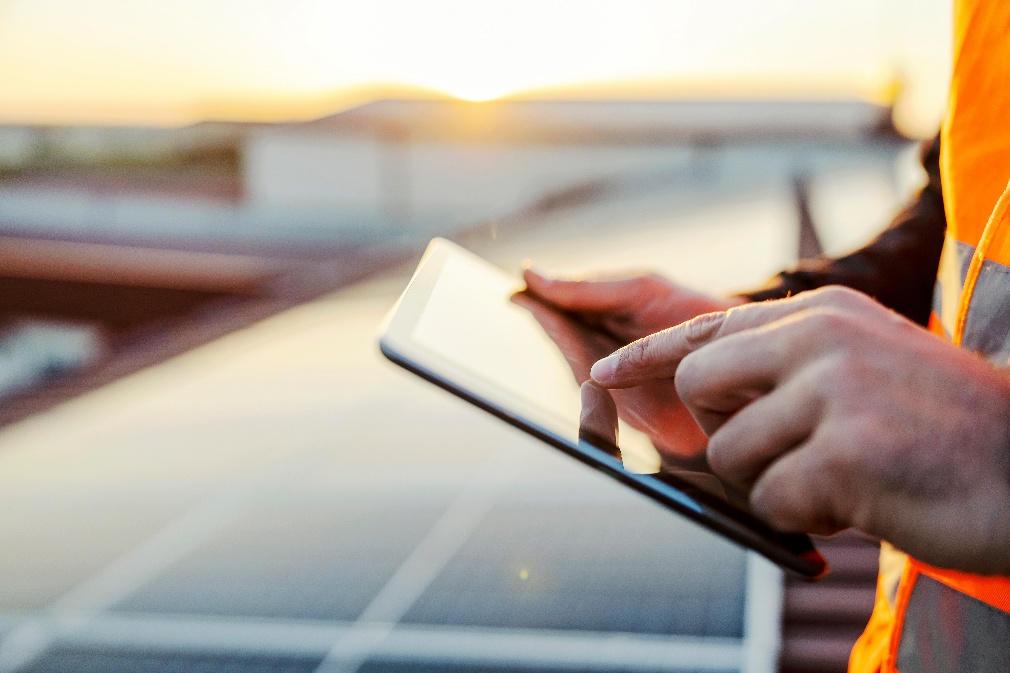 Engineer using a tablet in front of solar panels at sunset, representing AI and digital transformation in the energy industry.