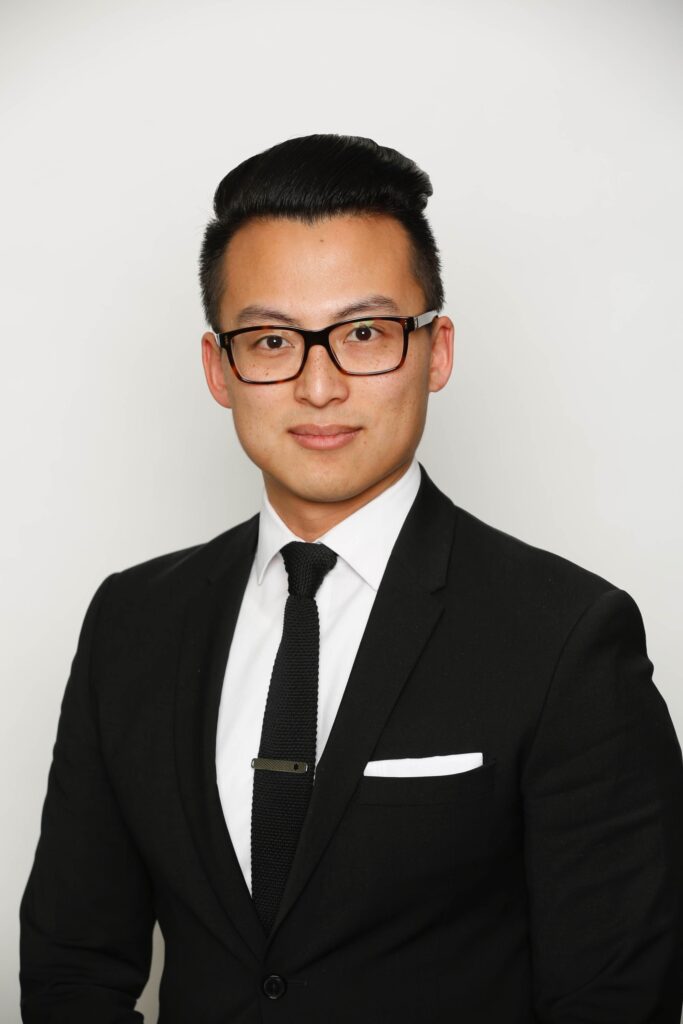 Keon Zhang, founder of the natural skincare brand Back To Earth, wearing a black suit and tie against a white background.