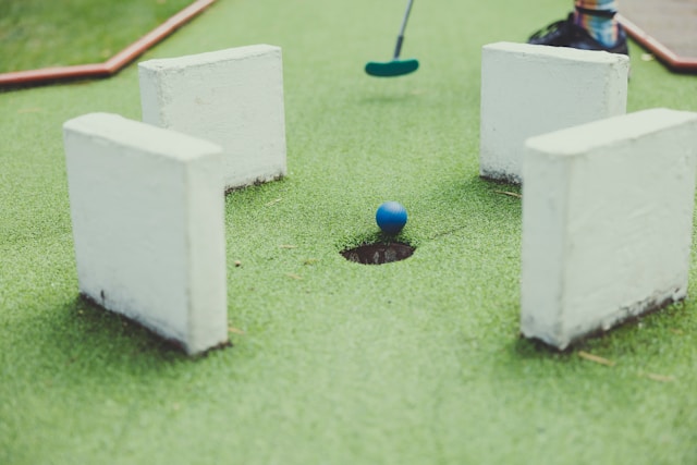 Blue golf ball about to drop into a mini-golf hole, demonstrating what to do with old golf balls for a fun backyard setup.