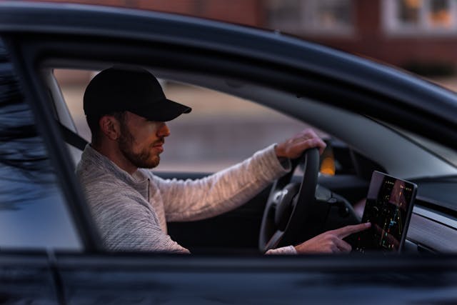 Man driving a Tesla and using the touchscreen system, highlighting how modern diagnostics work and answering the question: does Tesla have check engine light?