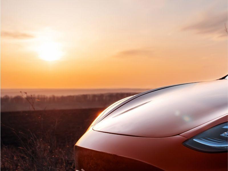 Close-up of a Tesla front under a sunset sky, symbolizing how Tesla regenerative braking work contributes to energy recovery during drives.