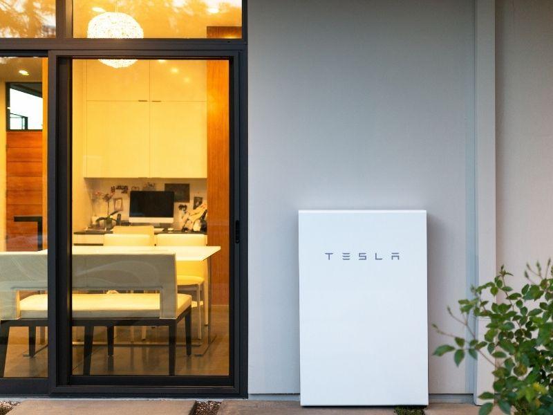 Tesla Powerwall mounted outside a contemporary home beside a sliding glass door, sparking the question: is the Tesla Powerwall worth it for reliable and sustainable home energy storage?