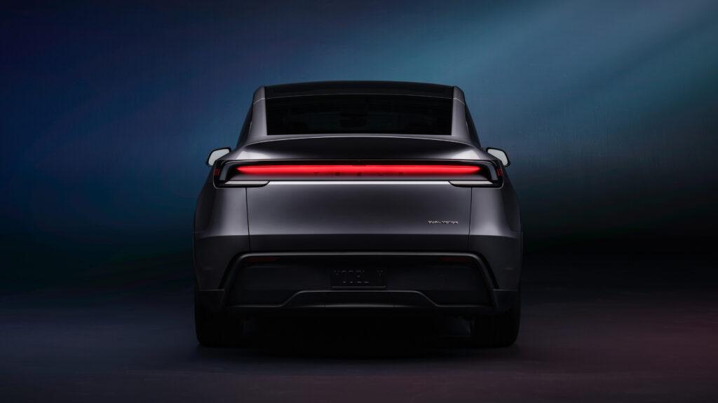 Rear view of a sleek Tesla Model Y against a dark gradient background, showcasing its minimalist design and full-width tail light in the context of audi q4 e tron vs tesla model y comparisons.