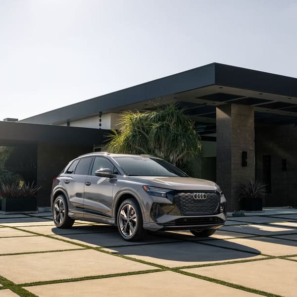 A sleek Audi Q4 e-tron SUV parked in front of a modern, minimalist house under a clear sky, representing a luxury EV choice in the audi q4 e tron vs tesla model y comparison.