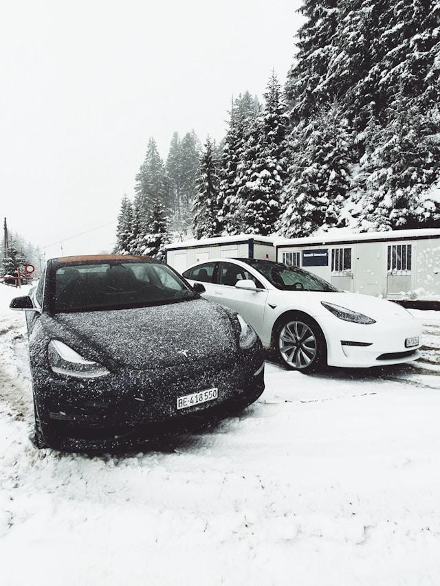 Two Tesla vehicles parked on a snow-covered roadside surrounded by snowy trees and portable buildings, illustrating the question: Is Tesla good in snow?