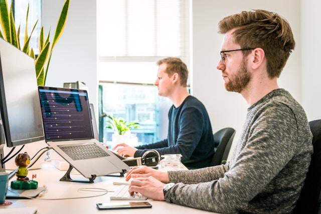Two young professionals working at computer desks in a bright, modern office, illustrating a typical work environment for individuals starting entry level jobs in nonprofit organizations, where collaboration and digital tools play a key role in daily operations.