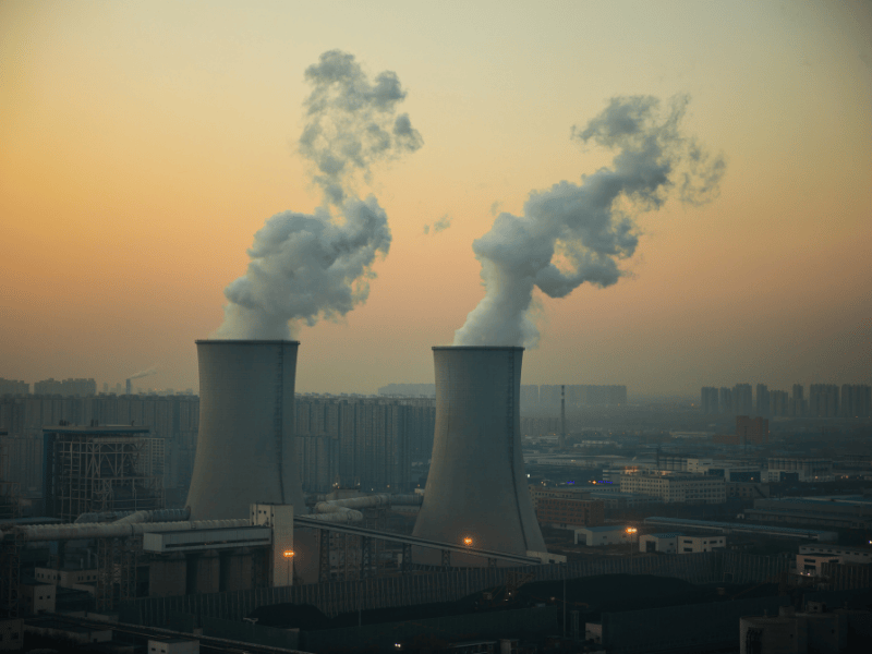 Coal power plant smokestacks emitting pollution into the air at sunset, illustrating the environmental impact of dirty energy in the United States.