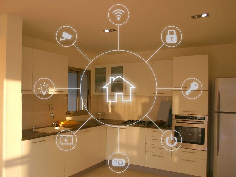 A modern kitchen illuminated by natural light, overlaid with a transparent smart home interface. The interface features icons representing home automation functions—such as lighting, security camera, door lock, power control, video surveillance, and key access—radiating from a central house icon. The image conveys the concept of integrating eco-friendly technologies for sustainable living through intelligent home systems.