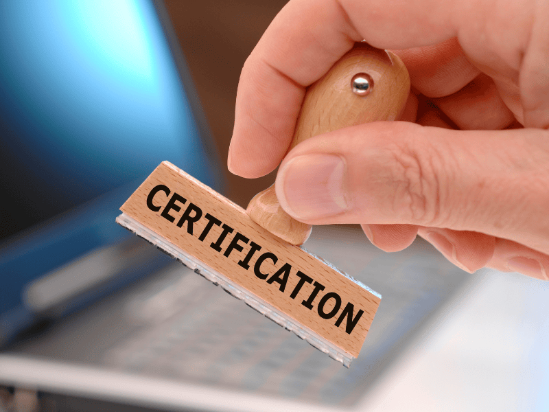 Close-up of a hand holding a wooden stamp labeled 'CERTIFICATION,' symbolizing the approval process for sustainability certifications in eco-friendly business practices.