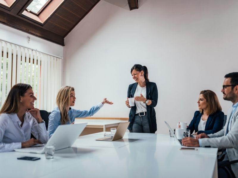 Group of diverse business professionals in a meeting room smiling and discussing ideas — concept related to what does D.E.I. stand for.