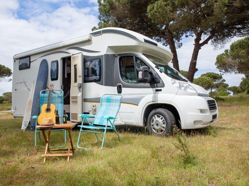 RV motorhome parked at a campsite with chairs and guitar outside, representing outdoor travel and the connection between Climate Change and Camping.