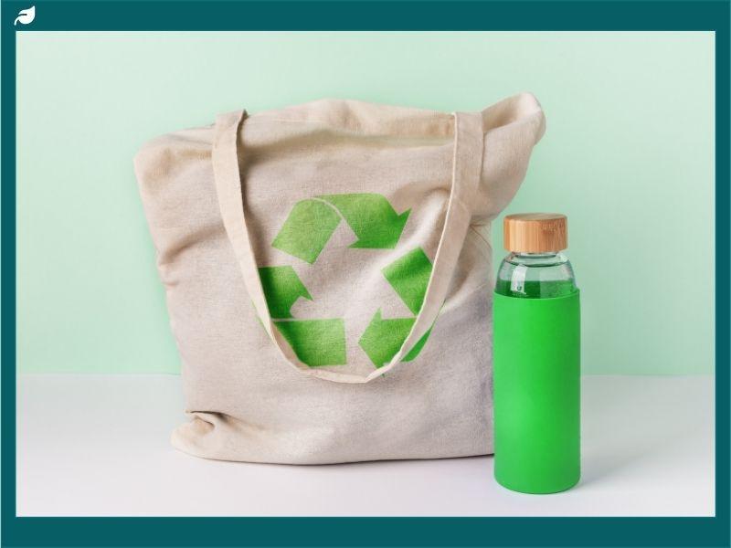eusable cloth bag with recycling symbol and eco-friendly water bottle, symbolizing Whole Foods reusable bag policy change and commitment to sustainability.
