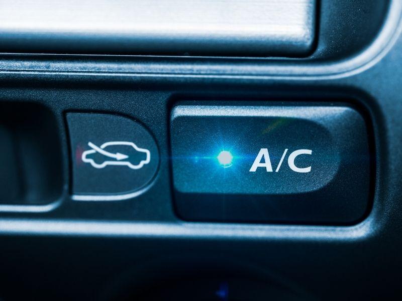 Close-up of EV air conditioning control button with illuminated A/C indicator inside an electric vehicle.