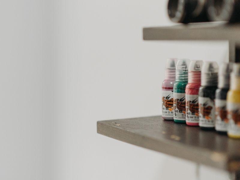Bottles of colorful tattoo ink on a shelf, representing safe and non-toxic ink for stick and poke tattooing.