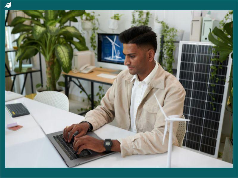Professional working on a laptop in a modern office with solar panel and wind turbine model.