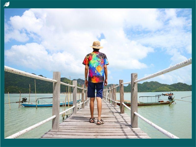 Traveler on a wooden pier overlooking boats and mountains, representing 2025 ecotourism facts and insights on sustainable travel and nature-based tourism.