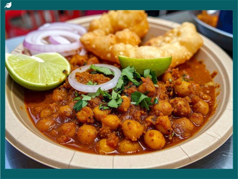Traditional Indian vegan dish of chickpea curry with fried bread, onions, and lime showcasing the variety and flavors of a vegan diet in India.