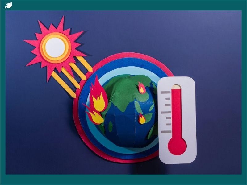 A paper-cut illustration of Earth surrounded by flames, a blazing sun, and a rising thermometer, symbolizing anthropogenic climate change and global warming caused by human activities.