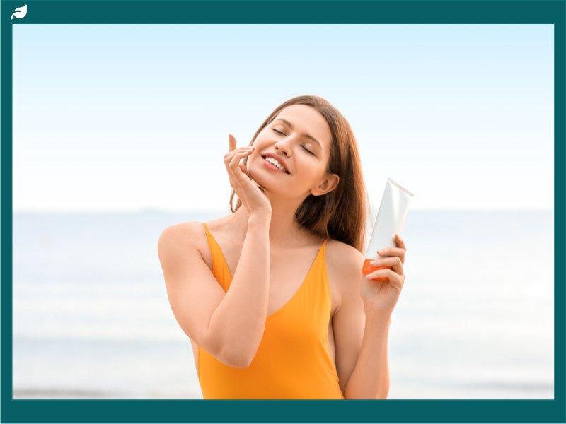 Woman applying sunscreen to face while standing on beach