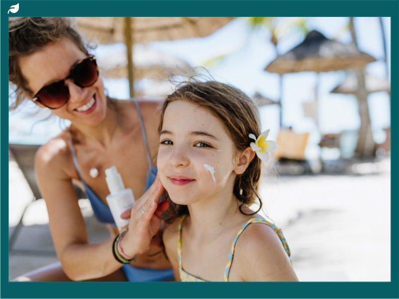 Mother applying sunscreen to young girl's cheeks beachside