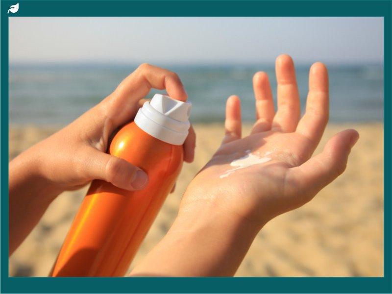 Hand spraying sunscreen from orange bottle at sandy beach