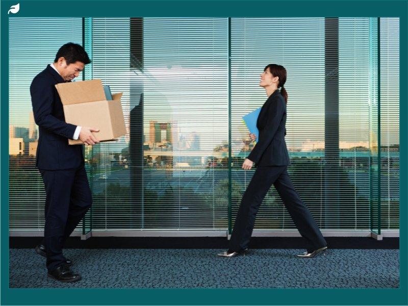 Man in suit carries cardboard box past colleague in office corridor