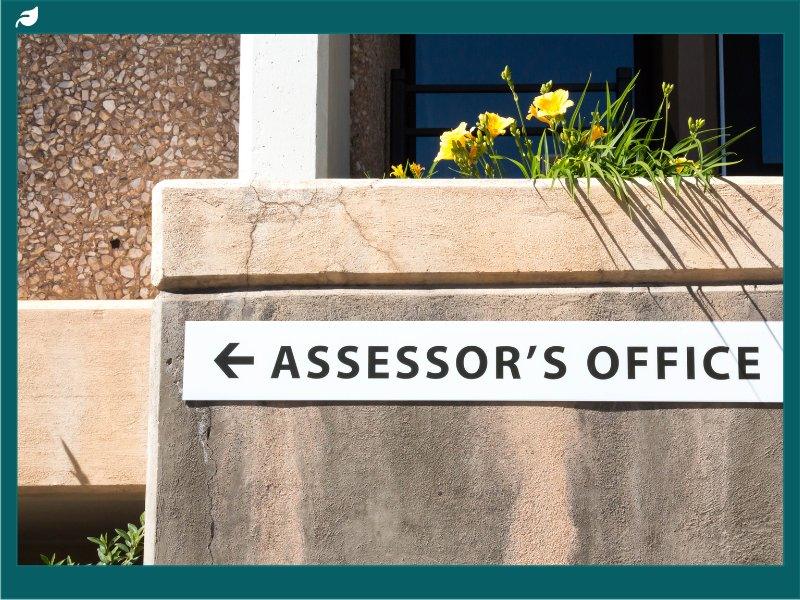Assessor's Office sign with arrow on sunlit stucco building wall
