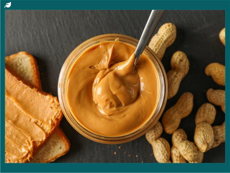Creamy peanut butter jar with spoon, toast, and shelled peanuts