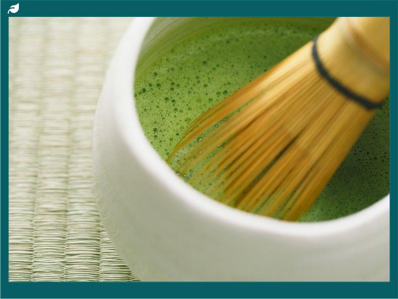 Bamboo whisk frothing bright green matcha tea in white bowl