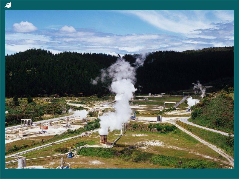 Geothermal power station releasing steam from wellhead pipes in valley