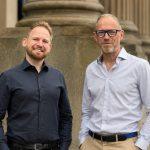 AECB Chief Executive Officer Ste Garlick and Chief Operating Officer Chris Iredale standing in front of a stone-columned building
