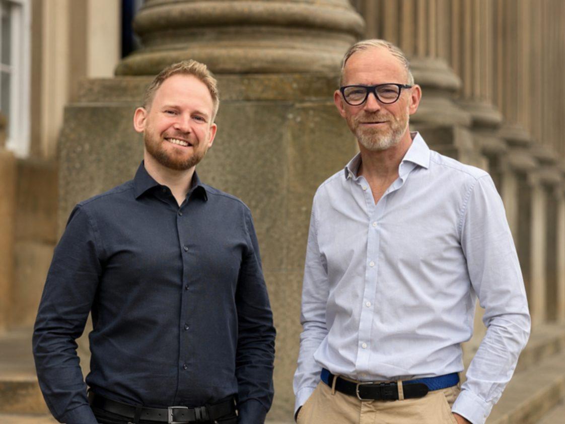 AECB Chief Executive Officer Ste Garlick and Chief Operating Officer Chris Iredale standing in front of a stone-columned building