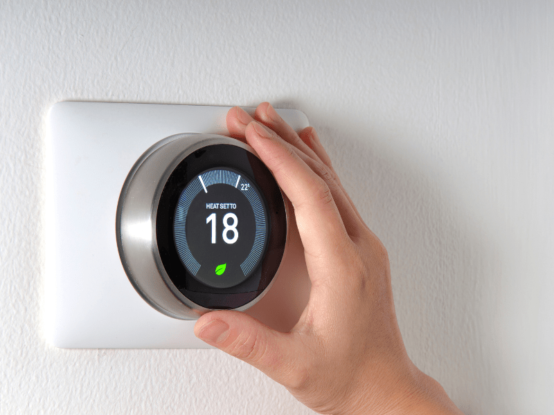 A hand adjusting a round smart thermostat set to 18 degrees
