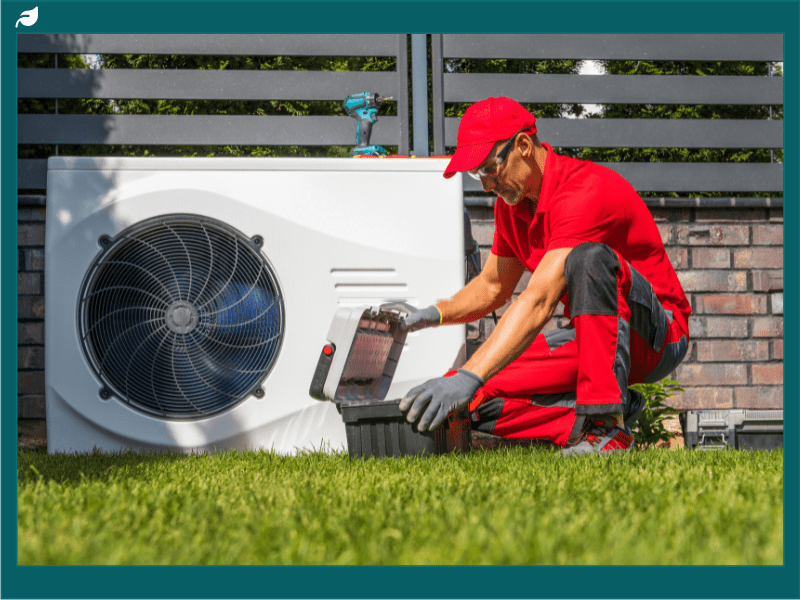 Man in red uniform installing white heat pump outdoor unit outside