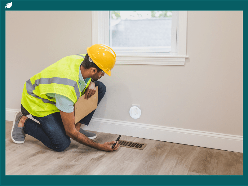 Inspector kneeling with clipboard checking air vent in home