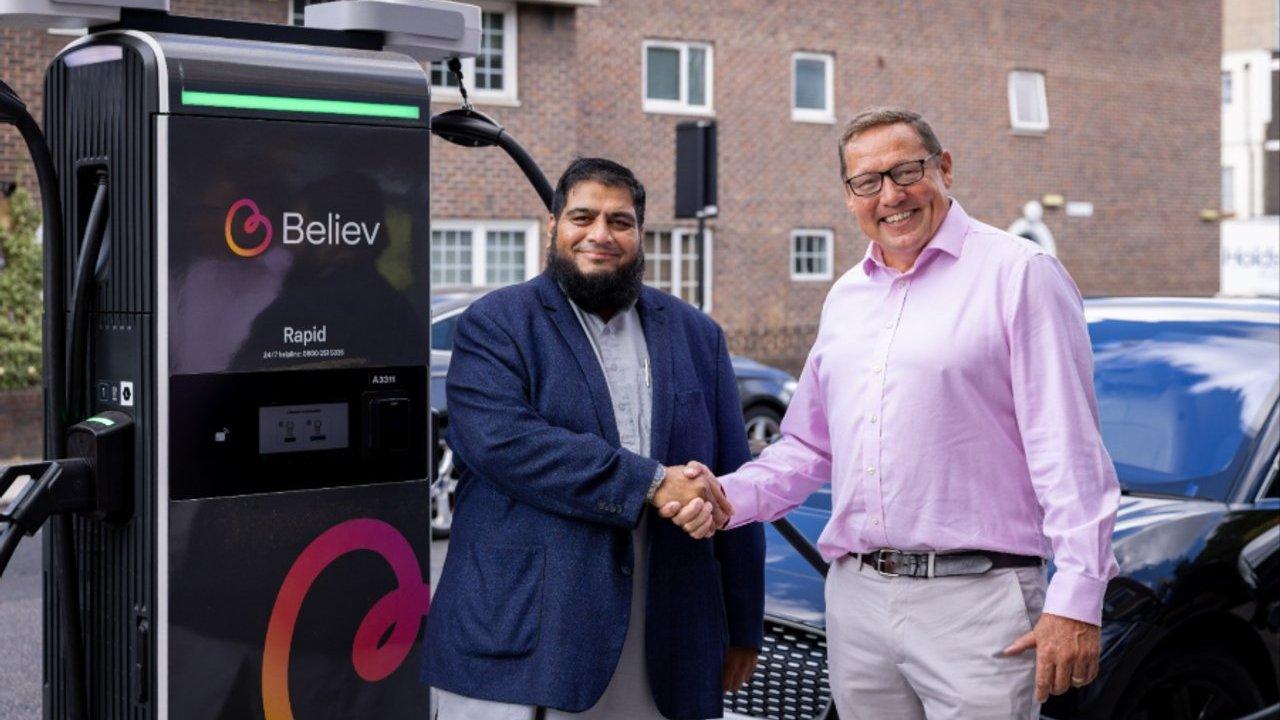 Two men shake hands beside a Believ rapid electric vehicle charging station and a parked car.