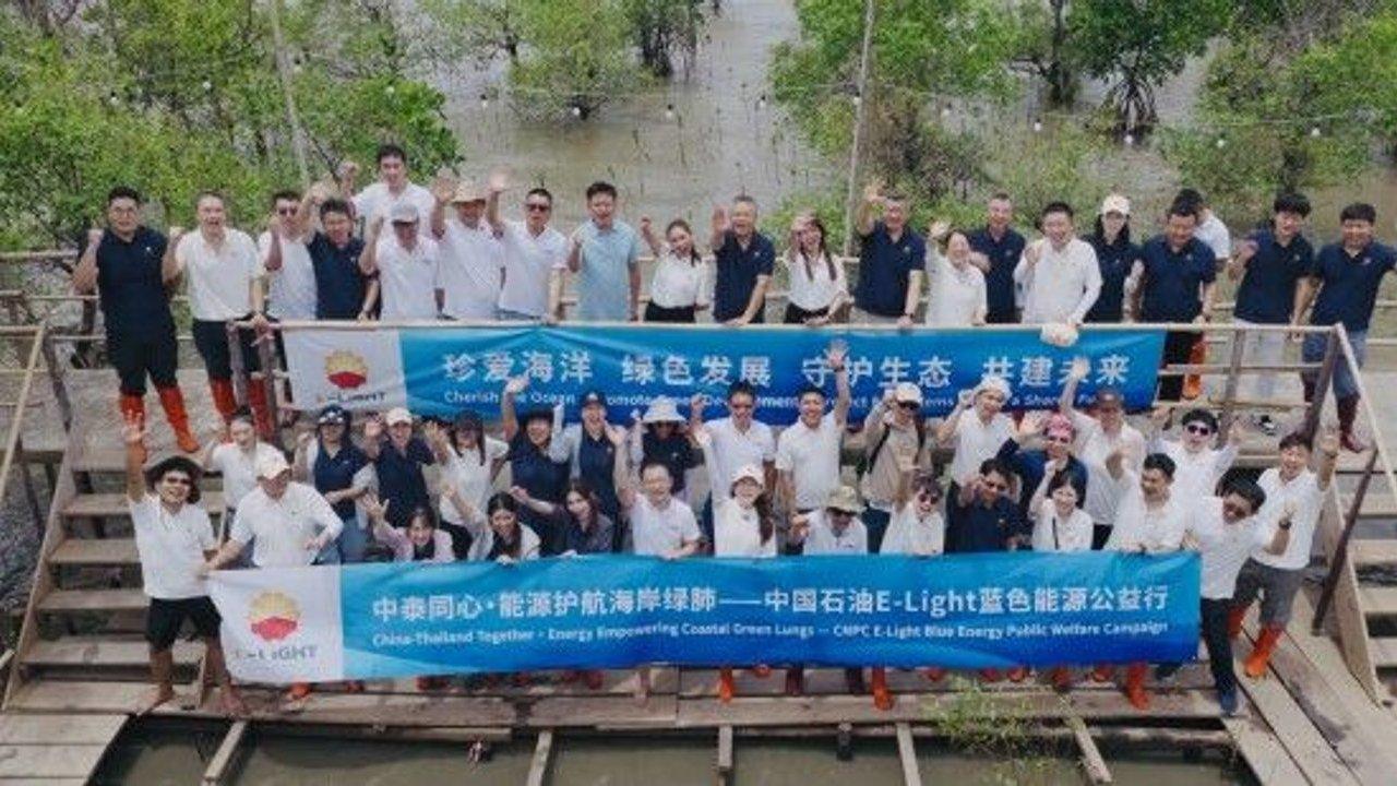 Group holding blue environmental campaign banners on a boardwalk in a mangrove wetland.